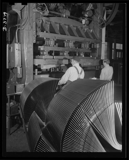 Stamping out parts for jeeps. Hood tops for army jeeps are stamped out on a 100-ton Hamilton press in a Midwest automobile plant. The standard hoods in the foreground were flat sheets a short time before. Ford Lincoln plant, Michigan