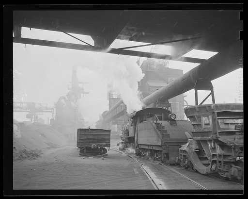 Steel production. Iron for our war machine. A busy blast furnace and the boiler house of another furnace are the background for a train of cinder ladles. Republic, Youngstown
