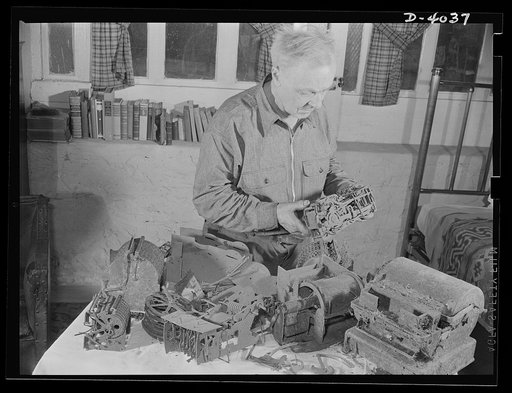 Dr. Bair. Scientist, now turned war worker, checks over fire-scarred models of some of his inventions. Dr. Bair, once a college professor and inventor, is aiding the production drive by sawing steel billets to sizes required by a large forging company. A fire destroyed his house and his valuable lib
