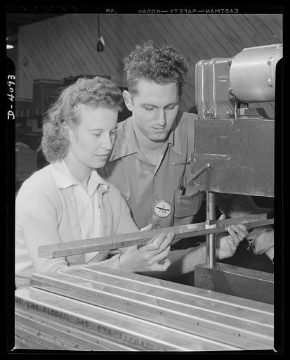 Women aircraft workers. Looks like "boy meets girl" in wartime and in war plants, but it's serious business here, for these two are among the hundreds of young people employed in a West Coast aircraft plant. He's a leadman and is instructing her in the use of a power rivet-squeezing machine