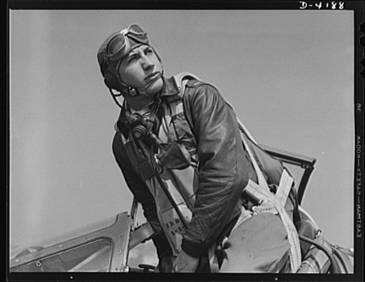 Mitchell Field. Eagle ready for battle. An American pursuit pilot in combat gear climbs into his plane. His flying equipment includes a combined oxygen mask and throat-type microphone, headphones, parachute and Mae West life jacket
