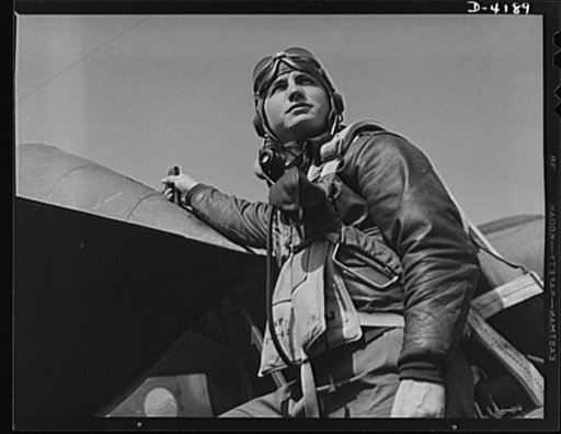 Mitchell Field. Eagle ready for battle. An American pursuit pilot in combat gear is all set to climb into his plane. His flying equipment includes a combined oxygen mask and throat-type microphone, headphones, parachute and Mae West life jacket