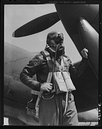 Mitchell Field. Eagle ready for battle. An American pursuit pilot in combat gear is all set to climb into his plane. His flying equipment includes a combined oxygen mask and throat-type microphone, headphones, parachute and Mae West life jacket