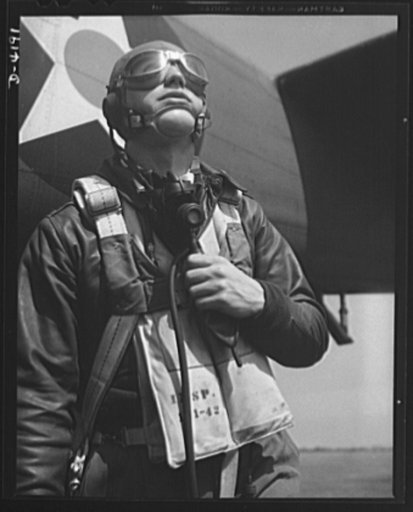Mitchell Field. Eagle ready for battle. An American pursuit pilot in combat gear is all set to climb into his plane. His flying equipment includes a combined oxygen mask and throat-type microphone, headphones, parachute and Mae West life jacket