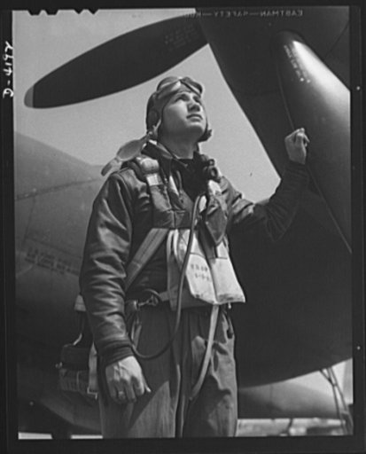 Mitchell Field. Eagle ready for battle. An American pursuit pilot in combat gear is all set to climb into his plane. His flying equipment includes a combined oxygen mask and throat-type microphone, headphones, parachute and Mae West life jacket