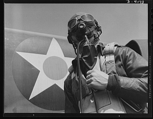 Mitchell Field. Eagle ready for battle. An American pursuit pilot in combat gear is all set to climb into his plane. His flying equipment includes a combined oxygen mask and throat-type microphone, headphones, parachute and Mae West life jacket