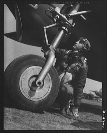 Mitchell Field. The eagle puts foot to earth. An air-crew officer dressed in full combat gear inspects a bomber landing wheel. Part of the retracting mechanism is shown