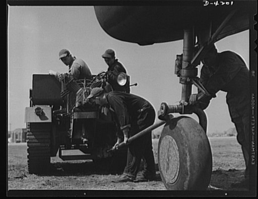 Mitchell Field. Air force tractor crew attach a towing link between a bomber and an airdrome tractor. The crew and tractor can handle the largest aircraft