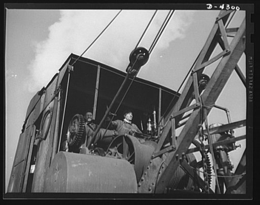 Production. Milling machines and machine castings. Masters of the open yard, the railroad crane man and his helper use a large electronic magnet to stack, sort and deliver scrap iron and steel to the overhead yard crane in the foundry