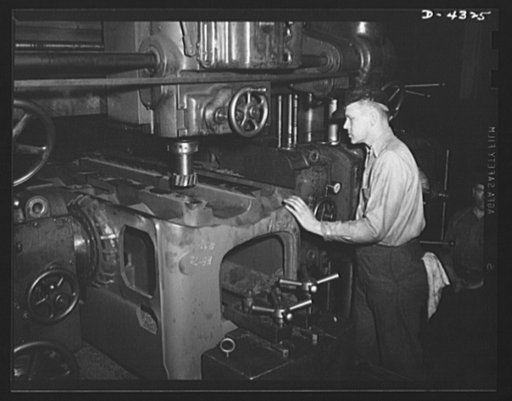 Production. Milling machines and machine castings. A close-up of a milling operation on a large bed. Note the multiple-touch cutter, larger than an elephant's foot, turning at the left. Facing it on the other side of the casting is another cutter of the same size, milling the other side. Special fix