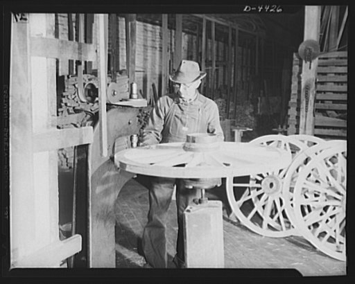Production. Wagon wheels. Revival of a dying art. A wheelwright in a Southern wagon plant operates a machine to insert bolts in the felly, or outer wooden rim of the wheel, prior to the fitting of the metal tire