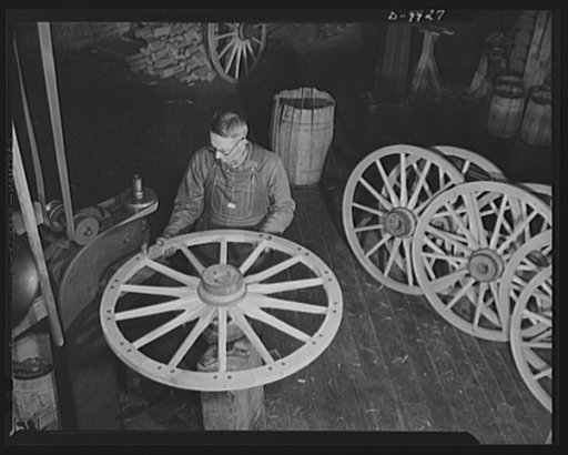Production. Wagon wheels. Revival of a dying art. A wheelwright in a Southern wagon plant operates a machine to insert bolts in the felly, or outer wooden rim of the wheel, prior to the fitting of the metal tire