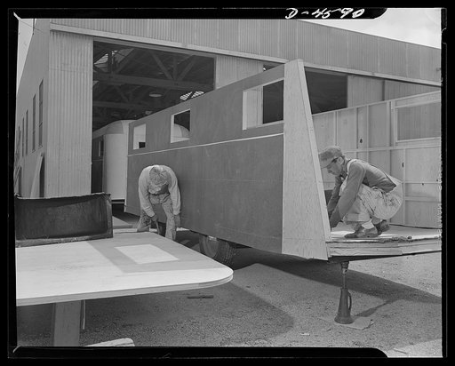Production. War housing trailers. A complete side assembly of a war housing trailer is set in place and secured at the Los Angeles plant of Western Trailer Company. At this stage, the trailer chassis is held on jacks to give stability and to make fitting of sections fast and accurate
