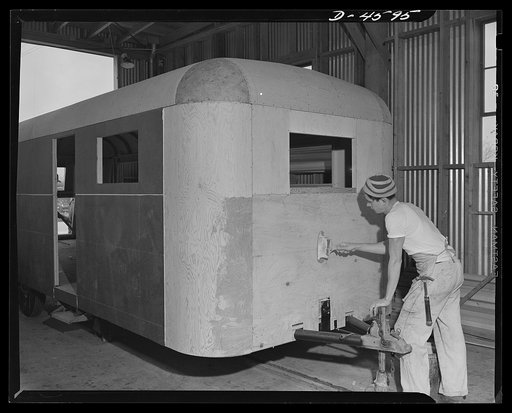 Production. War housing trailers. Men on the assembly line of Western Trailer Company are assigned by stations and perform the same series of tasks on successive trailers. Here, a front end receives a treatment of casein glue over which Masonite will be applied