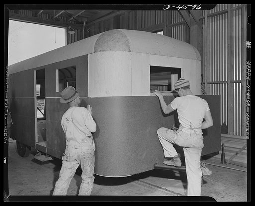 Production. War housing trailers. Masonite board is bent into position and carefully lined up on the plywood body of a war housing trailer being built at Los Angeles by Western Trailer Company. Nails and drive screws are used in addition to glue