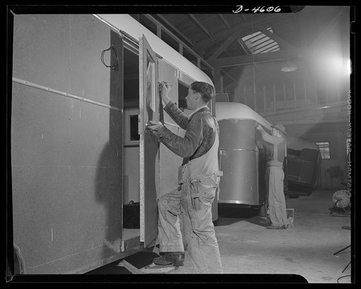 Production. War housing trailers. The trailer door is the last major assembly to be fitted to a war housing trailer at the Los Angeles plant of Western Trailer Company. The worker in the background is installing clearance light fittings. The vehicle is now ready for the final paint job