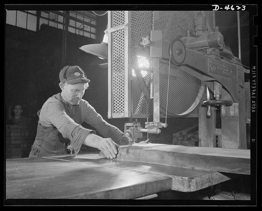 Conversion. Flooring to gunstocks. Cutting gunstock blocks for the Army. A walnut slab, or flitch, is run through a band saw, and marked sections are cut out with precision. The final clear pieces, of gunstock dimension, will later be cut from these sections by the ripsaws of a converted flooring pl