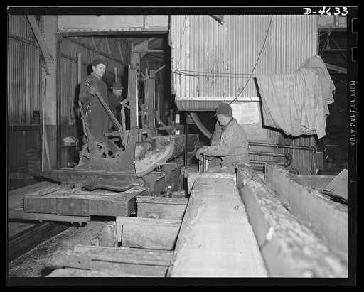 Production. Veneer for aircraft and other war essentials. Sawmill carriage in a large Midwest veneer plant cuts flitches, or slabs, from an oak log that will be used in making veneer for essential war purposes. The sawyer at the right controls the speed of the carriage and the thickness of the cut. 