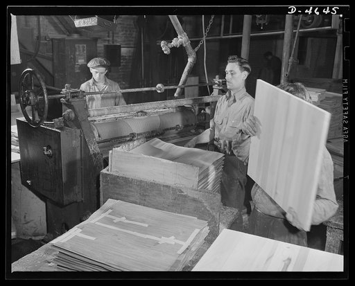 Production. Plywood for aircraft and boats. Strong, light plywood for our fighting planes. An exact and even spread of urea glue is applied by machine onto the crossboards of lumber-core panels to permit attaching of wood veneers in a Midwest plant. Louisville, Kentucky