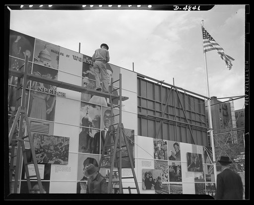 Four Freedoms and Arsenal of Democracy posters. With the final section still to be placed on the scaffolding, a worker is already installing the wiring for the two 15 x 30 foot photomontages displayed in Defense Square, Washington for a month beginning November 7, 1941. The panels, entitled The Four