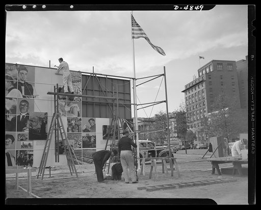 Four Freedoms and Arsenal of Democracy posters. With the final section still to be placed on the scaffolding, a worker is already installing the wiring for the two 15 x 30 foot photomontages displayed in Defense Square, Washington for a month beginning November 7, 1941. The panels, entitled The Four