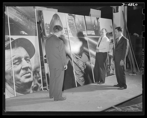 Part of the Arsenal of Democracy panel designed by Jean Carlu, eminent poster artist, for the Office of Emergency Management (OEM) and seen first at the National and Civilian Defense Exposition in New York's Grand Central Palace. Mr. Carlu, in shirtsleeves, is explaining his new technique in photomo