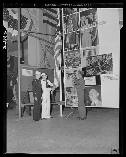 Protectors of the Four Freedoms raise Old Glory by the Office of Emergency Management's (OEM) huge Four Freedoms photomontage at the National and Civilian Defense Exposition in Grand Central Palace, New York. This panel, which measures 15 x 30 feet, and another of equal size entitled Arsenal of Demo