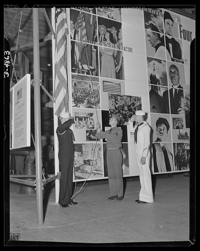 Protectors of the Four Freedoms raise Old Glory by the Office of Emergency Management's huge Four Freedoms montage at the Natinoal Civilian and Defense Exposition in Grand Central Palace, New York. This panel, which measures 15 x 30 feet, and another of equal size entitled Arsenal of Democracy, were