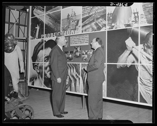 "Open the doors," says Jean Carlu, eminent poster artist, to Manager Sloan of the National and Civilian Defense Exposition at New York's Grand Central Palace. In the background is part of the 15 x 30 foot poster Carlu designed for the Office of Emergency Management (OEM). The panel shown represents 
