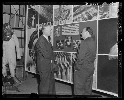 "Open the doors," says Jean Carlu, eminent poster artist, to Manager Sloan of the National and Civilian Defense Exposition at New York's Grand Central Palace. In the background is part of the 15 x 30 foot poster Carlu designed for the Office of Emergency Management (OEM). The panel shown represents 