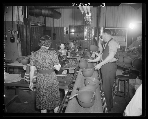 Conversion. Auto radiators to army helmets. Steel helmets for the Army travel down a conveyor in a converted Eastern auto radiator plant. Men and women inspectors check the finished helmets. McCool Radiator Company, Detroit, Michigan
