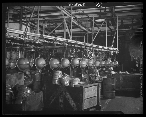 Conversion. Auto radiators to army helmets. Steel helmets for the Army. Continuous chain conveyors in the stamping department of a converted auto radiator plant where presses form helmets from sheet steel and trim them at the edges. McCool Radiator Company, Detroit, Michigan