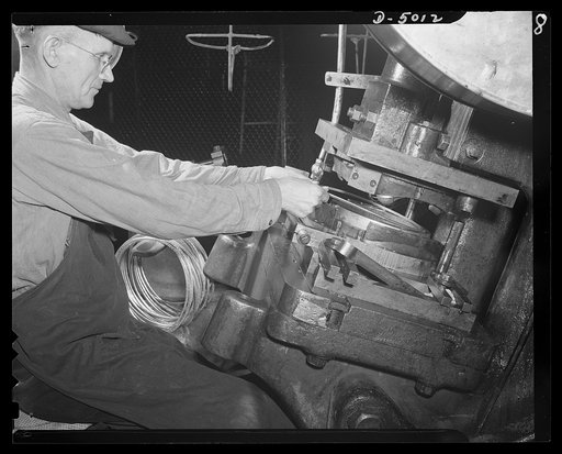 Conversion. Auto radiators to army helmets. Joining a steel reinforcing rim on an army helmet. The stamping press that performs this operation is one of many that formerly turned out auto radiator parts for an Eastern manufacturer. McCool Radiator Company, Detroit, Michigan
