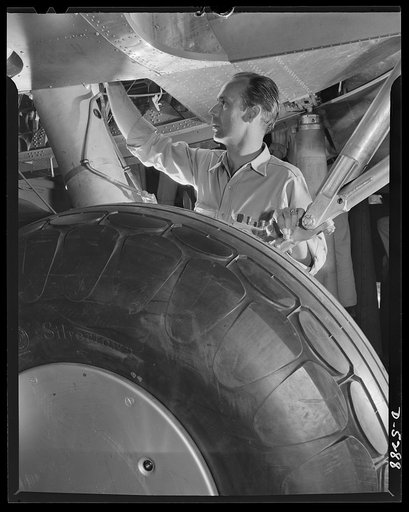 Production. Aircraft. At the end of a Flying Fortress assembly line, this mechanic in a large Western plant makes a final check on a landing gear hydraulic system. That big round object in the foreground is a rubber tire. Remember?