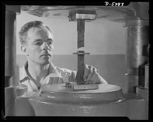 Production. Aircraft. An engineer in the laboratory of a large Western aircraft plant tests a standard Army weld sample. At irregular intervals every welder working on Army contract material must make the "tee" weld shown here. This sample has failed, as part of the break has occurred in the weld ra