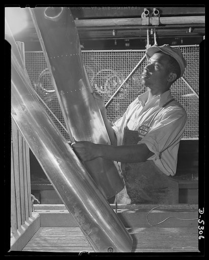 Production. Aircraft. A Negro worker in the metal-treating division of a large Western aircraft plant passes structural sections along the line for further processing and assembly