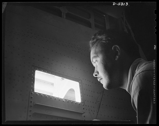 Production. Aircraft. With the aid of a powerful light, a Lockheed inspector checks rivets in all but the inaccessible wing section of a YP-38 plane wing
