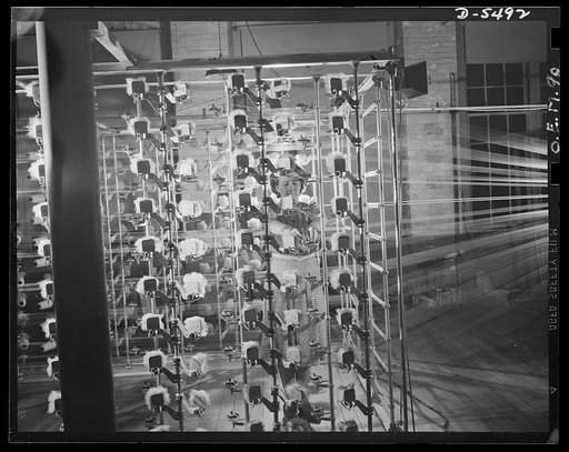 Production. Parachute cloth and shrouds. Warping nylon threads for use in the manufacture of parachute cloth in an Eastern plant. A close-up of the warping machine, showing how the spools of nylon are supported
