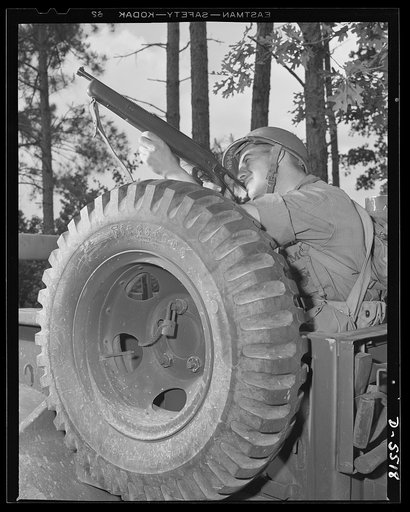 New River, North Carolina. Marine truck convoy. When a leatherneck gets a tommy gun lined up, something is due to be hit. Bulwarked by a spare tire, this capable member of a Marine Corps truck convoy goes in for a little practice with a submachine gun as his column halts on a training cruise near Ne