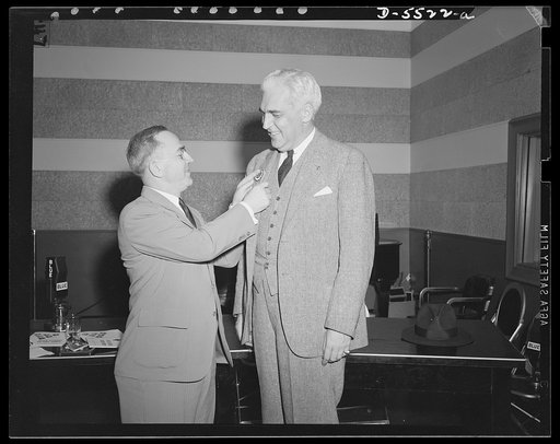 Scene at the first broadcast announcing the formation of high school Victory Corps throughout the U.S. Broadcast was made over station WMAL, Washington, D.C. on September 25, 1942 from 8:30 to 9:00 p.m. EWT. John W. Studebaker, U.S. Commissioner of Education, places emblem on Paul V. McNutt, Chairma