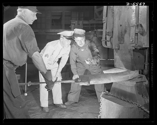 A poster comes to life. K.P. was nothing like this, thinks Sergeant Vineyard, squinting against the scorching air which rises from the forging of a crane hook. Steel worker George Woolslayer (right) tells the Sergeant how his fellow workers go about the forging of implements of war in a blacksmith s