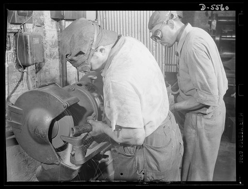 Industrial safety. Accident prevention. A safe grinding job. Both operator and helper are protected by proper goggles and the exhaust hood over the grinding wheel carrying away the greater part of the ground-off particles. Each man is very careful to sterilize goggles that have been worn by other wo