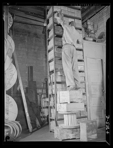 Industrial safety. Accident prevention. This shop worker is "asking for it." The use of a makeshift "ladder" like this is always hazardous--doubly so when heavy, bulky, or unwieldy objects are being put in place or removed