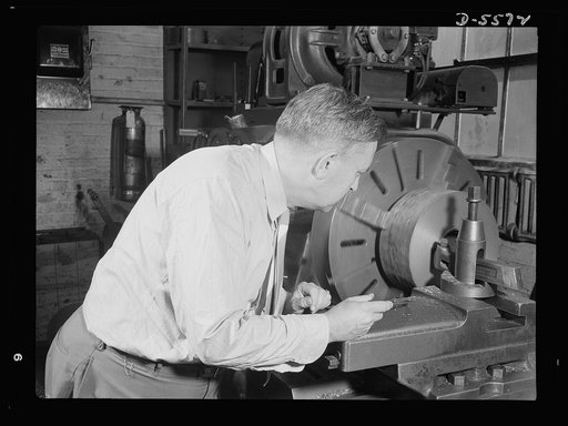 Industrial safety. Accident prevention. This man is violating two rules of good plant practice: he is fooling around with machinery unfamiliar to him and he is wearing unsuitable and dangerous clothing. His tie might easily get caught in the moving machinery