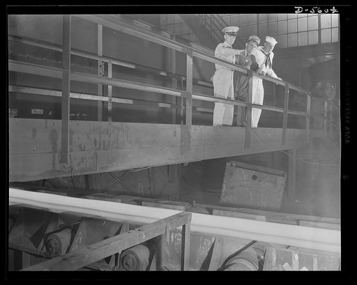 A poster comes to life. Squinting against the terrific glare and bursts of steam charging up from a strip of red-hot steel which moves slowly past them, Sergeant Vineyard and Chief Evans pause with welder Woolslayer to watch precious river, which comes off the blooming mill and rolls toward the four