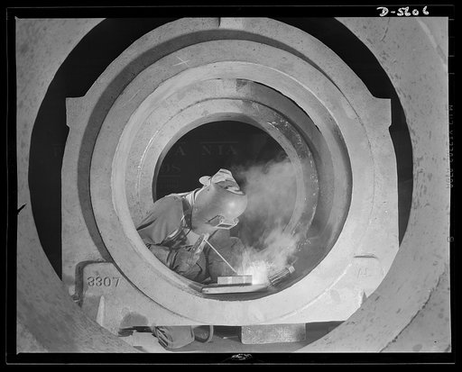 A poster comes to life. Meet an American soldier of Production. George Woolslayer, thirty-two-years-old, is an experienced welder at one of Allegheny-Ludlum's steel mills. His uniform is a pair of overalls and a welder's mask. Not reveille but a battered alarm clock awakens him six days a week at 6 