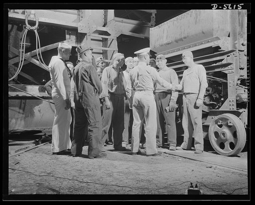 A poster comes to life. "Meet the guys who shoot 'em." George Woolslayer introduces a group of open-hearth furnace men to his poster pals, Evans and Vineyard, who are getting a first-hand view of production for war. Although they knew how to shoot guns and drive jeeps before they came to Allegheny-L