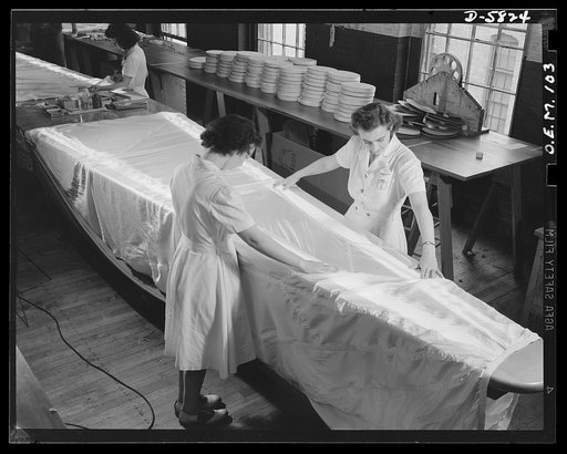 Production. Parachute making. Though it looks like a skirt on an ironing board, this is really a parachute stretched over a glass table, upon which it is subjected to rigid inspection. Electric lights underneath the table show up the slightest imperfection. Pioneer Parachute Company, Manchester, Con