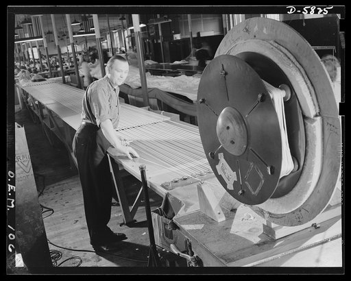 Production. Parachute making. What a boomerang these shroud lines may turn out to be! Made partly from Japanese silk, they are being layed out for marking and cutting. The marker is Charles Baggott, at one time an English butler at the British Embassy in Washington. The parachutes he is helping to p