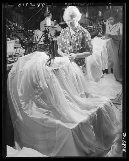 Production. Parachute making. Not taking a tuck in a wedding gown but sewing up a seam of a flare parachute! This is a joining operation in which sixteen panels, or gores, of the parachute are sewn together. Pioneer Parachute Company, Manchester, Connecticut